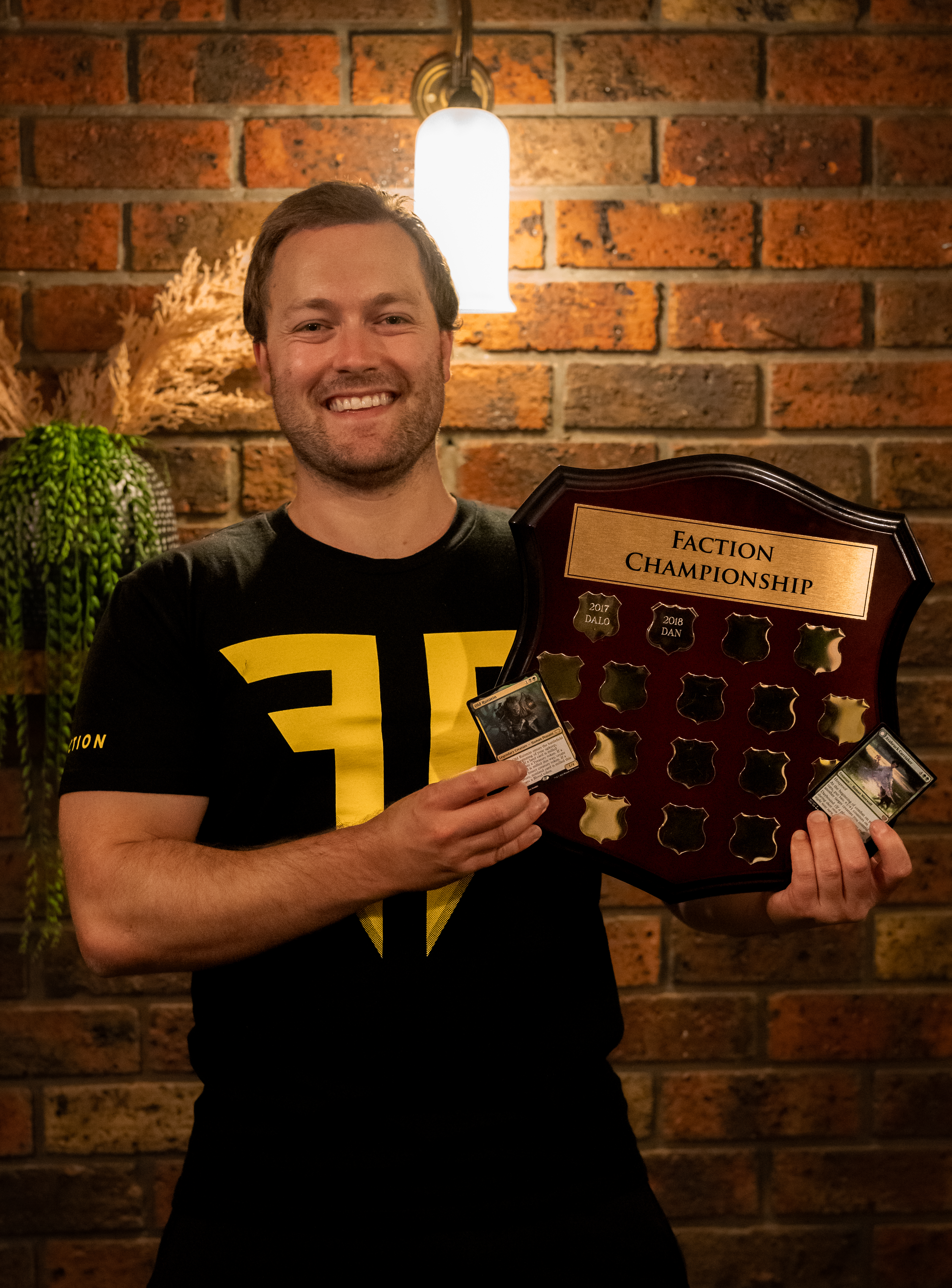 Alex Crowther poses with the Faction trophy and a pair of Magic cards